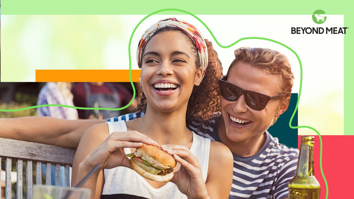 A young man and woman smiling while holding a beer and a hamburger