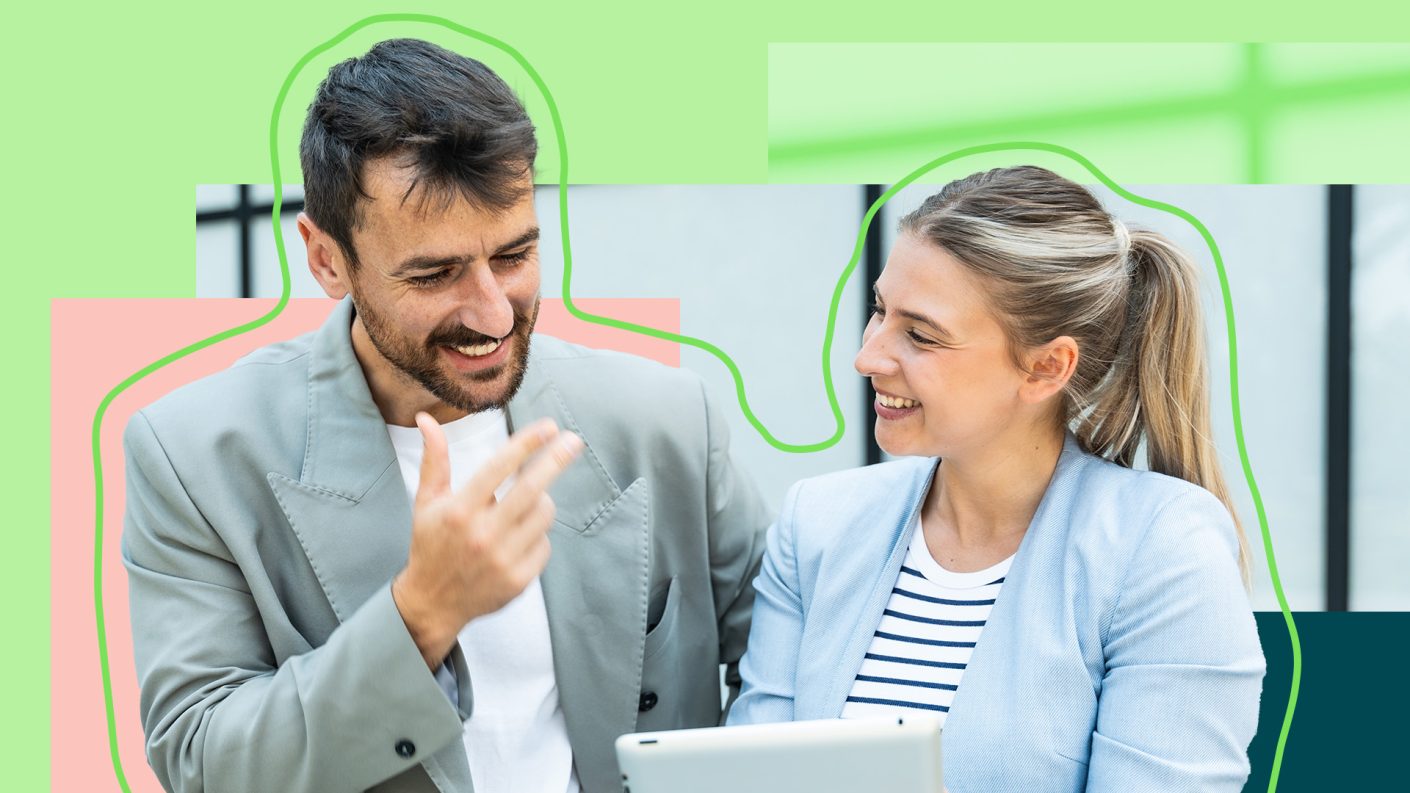 Business man with dark hair and business woman with blond hair smiling and having a discussion over a tablet.