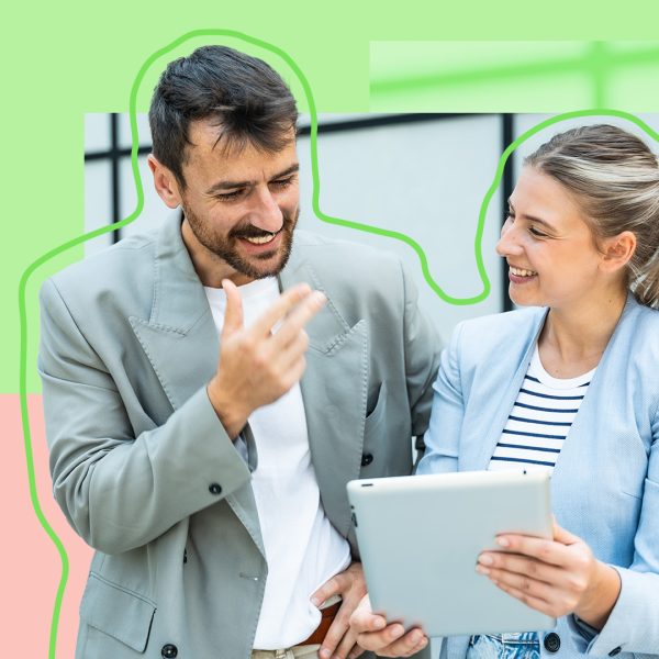 Business man with dark hair and business woman with blond hair smiling and having a discussion over a tablet.