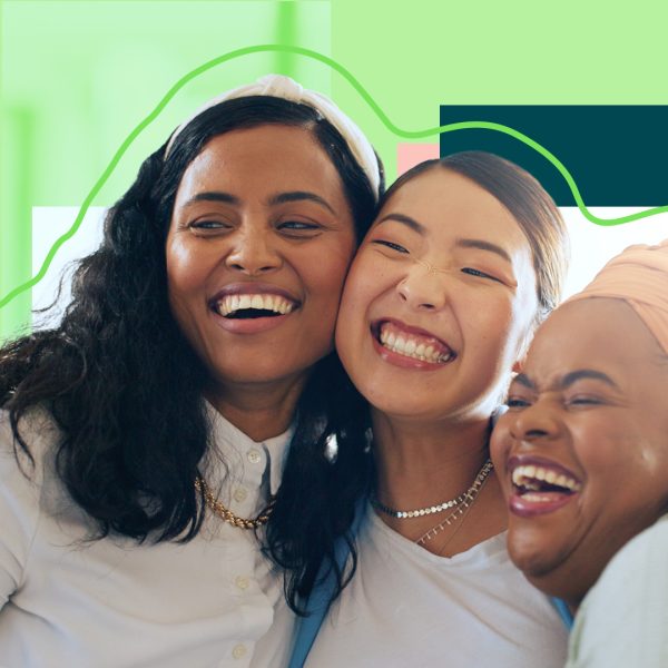 Three women hugging and smiling on a green background.