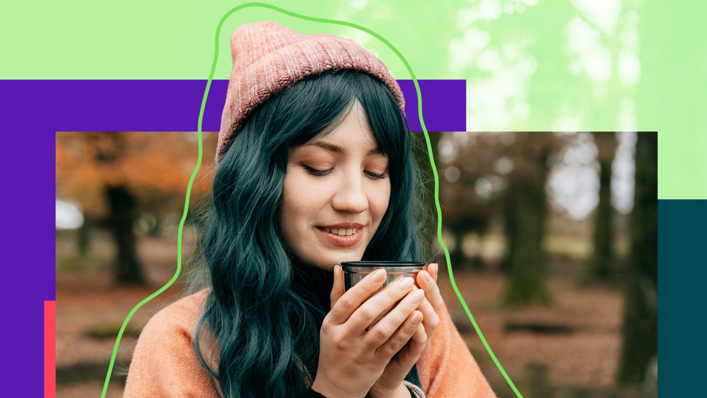 Woman in a pink sweater and hat warming her hands on a cup of coffee