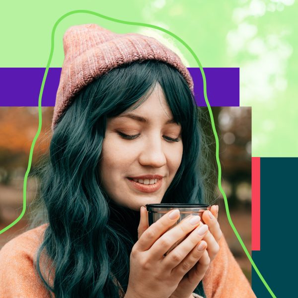 Woman in a pink sweater and hat warming her hands on a cup of coffee