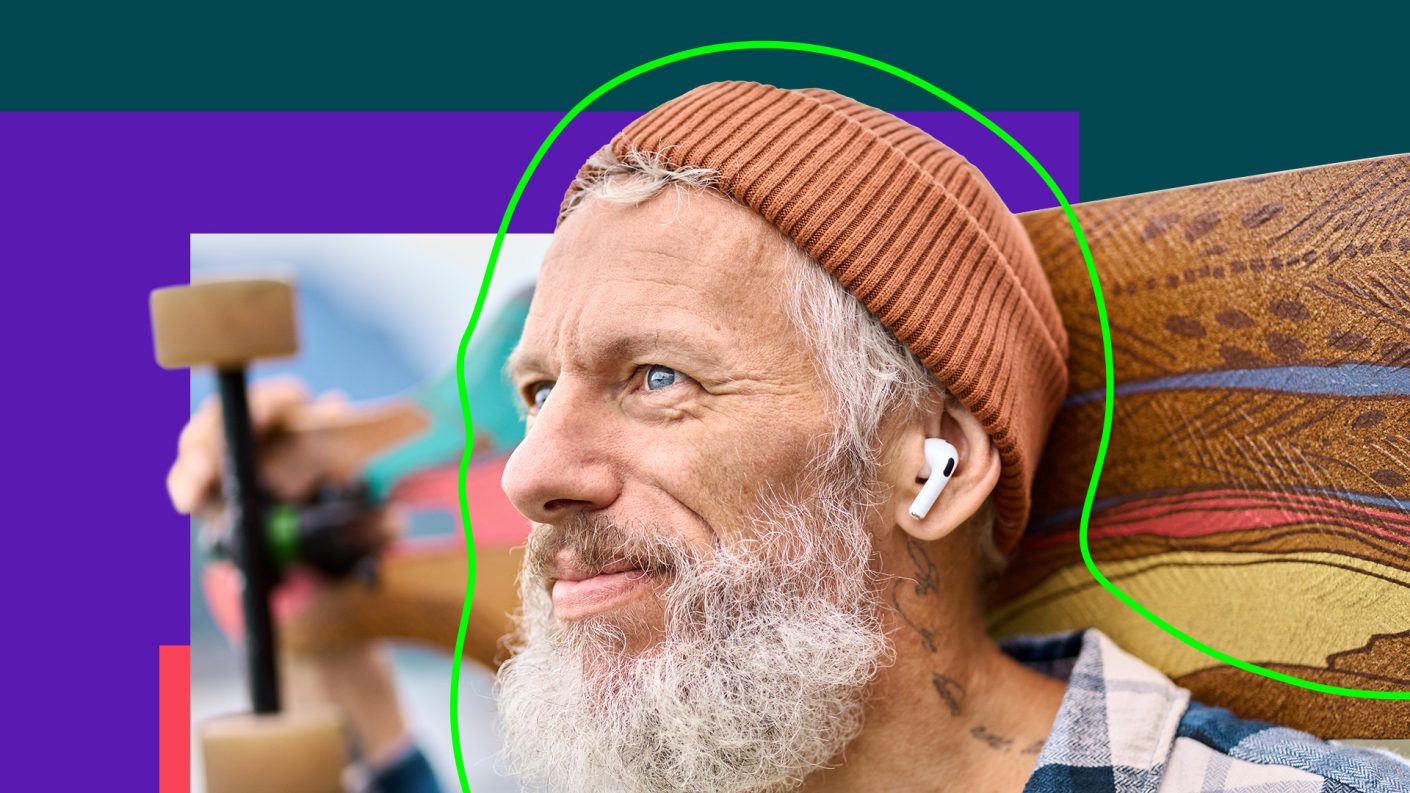 Person with grey hair and beard wearing a skateboard on his shoulders.